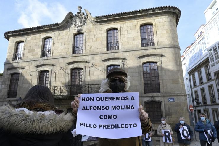 Un home leva un cártel no que se le, `Non queremos a Alfonso Molina como fillo predilecto´, xunto a varias persoas que se concentran fronte á Casa Cornide baixo a lema 