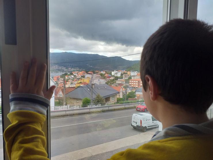 Un neno observa a rúa desde o interior da súa casa, en pleno confinamento polo estado de alarma decretado con motivo da pandemia de coronavirus 