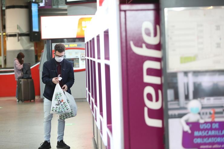 Un viaxeiro con máscara obtén un billete nun dispensador dunha estación de tren de Renfe 