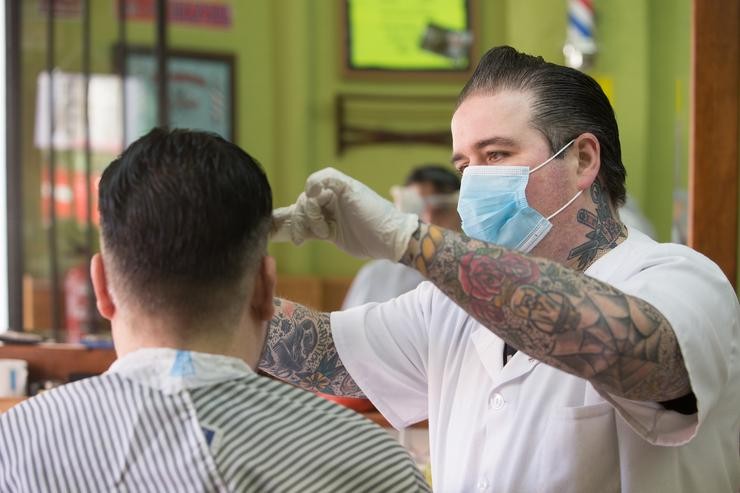 Un empregado da barbaría Rockabilly Memphis, aberta durante o día 51 do estado de alarma, peitea o pelo a un cliente, en Lugo 