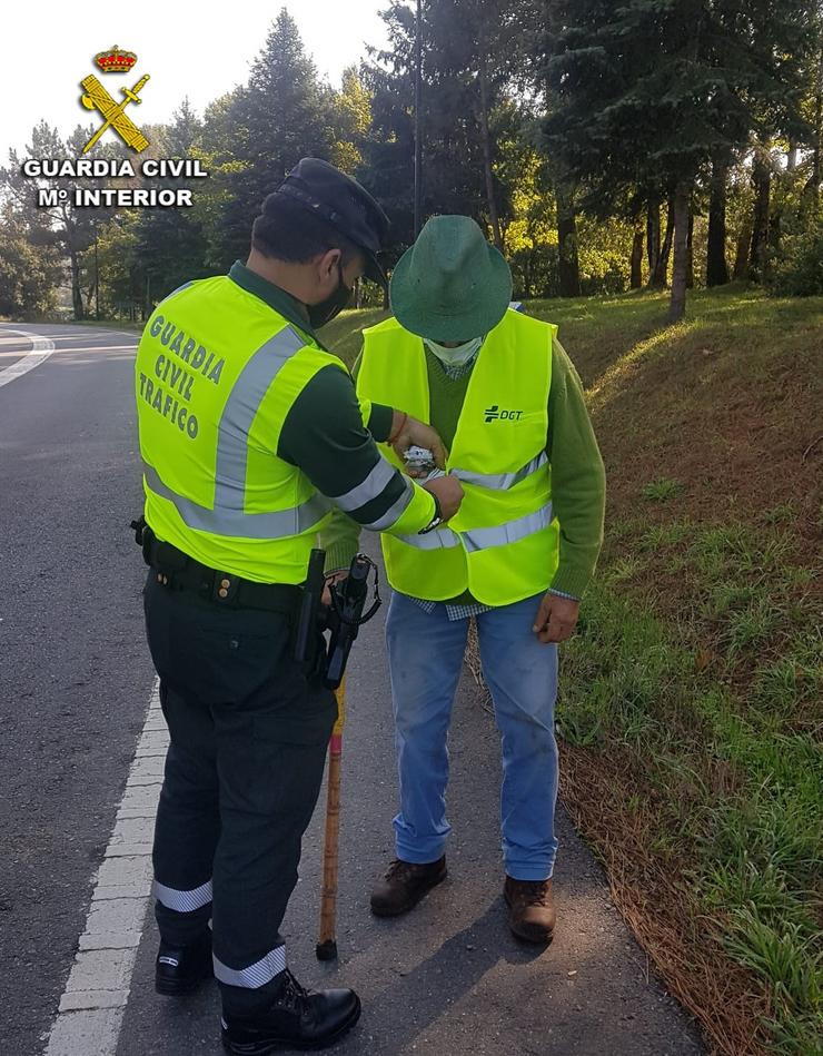 Un garda civil coloca un chaleco reflector ao home auxiliado. GARDA CIVIL