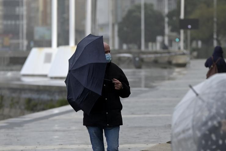 Un home cun paraugas camiña polo paseo marítimo mentres chove, a 8 de decembro de 2021, na Coruña, Galicia, (España). A borrasca Varra fixo que a Xunta haxa activado para todo o litoral galego unha alerta laranxa por temporal costeiro. S. M. Dylan - Europa Press 