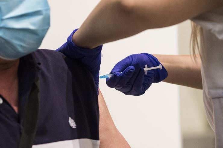 Unha sanitaria administra a primeira dose da vacina de Pfizer contra a covid-19 a un home 