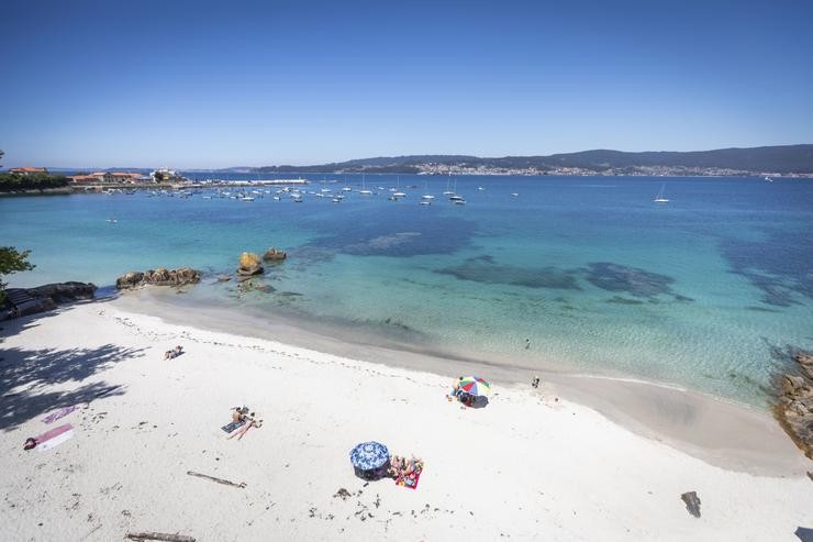 Varias persoas báñanse e toman o sol nunha praia de Marín 