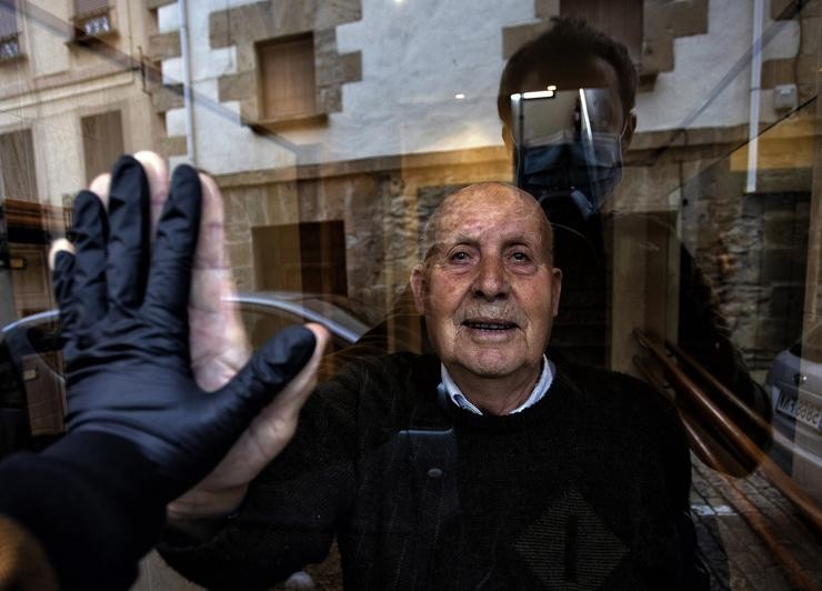 'Visita ao meu avó Miguel, de 90 anos, durante o confinamento, que saúda a través do cristal do portal,  Huarte, Navarra, 1 de abril, 2020'. (© Unai Beroiz 