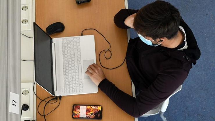 Estudante cun teléfono móbil e un ordenador