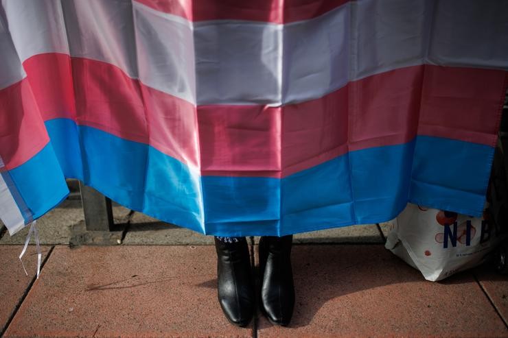 Os zapatos dunha persoa debaixo dunha bandeira trans. Alejandro Martínez Vélez - Europa Press