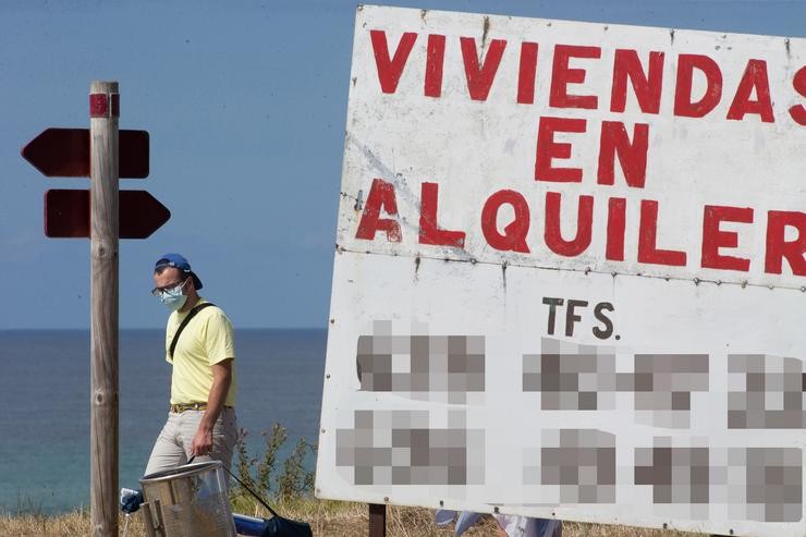 Un home camiña xunto a un cartel de vivendas en aluguer na Mariña / Carlos Castro