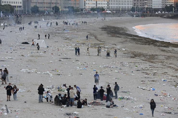 Vista xeral da praia de Orzán con grupos de persoas e restos de lixo despois da celebración das fogueiras da noite de San Juan.. M. Dylan - Europa Press / Europa Press