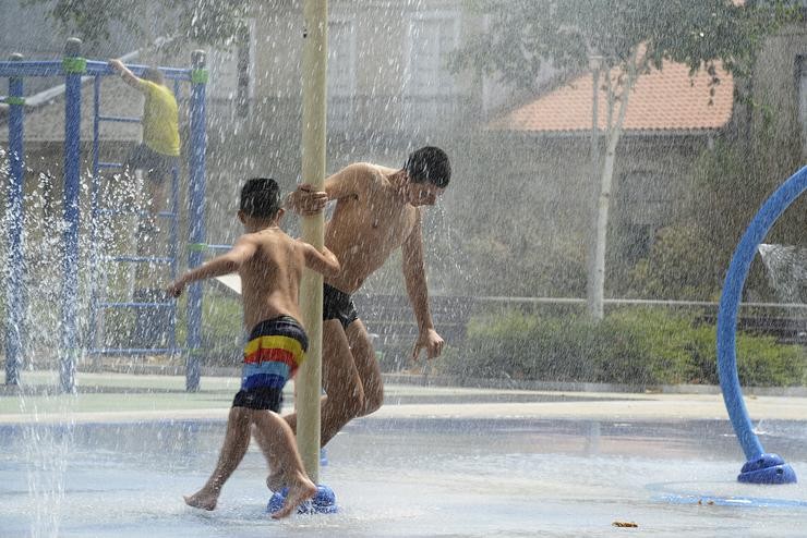 Dúas persoas refréscanse nuns chorros durante un día de calor en Ourense 