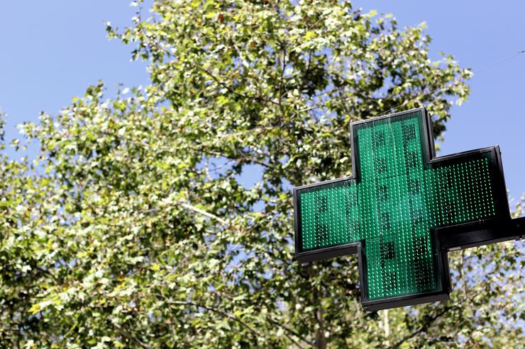 Un sinal luminoso da cruz verde á entrada dunha farmacia 