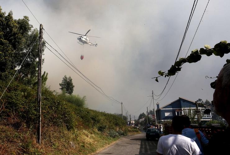 Un helicóptero entre o fume, traballa cunha cuba de auga no incendio, a 22 de agosto, na parroquia de Meira, en Moaña, Pontevedra, Galicia (España). O lume declarado nunha zona de eucaliptos, obrigou a cortar a autovía do Morrazo entre l. Javier Vázquez - Europa Press