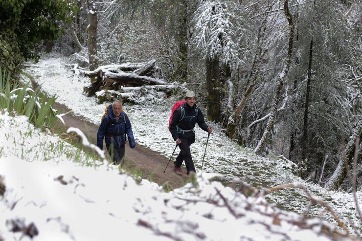 Dous peregrinos camiñan na neve polo pobo prerromano do Cebreiro 