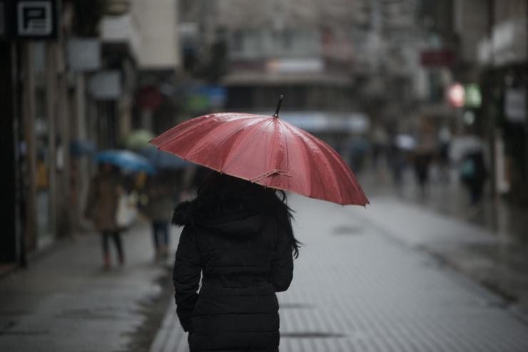 Unha persoa con paraugas para protexerse da choiva camiña pola Rua Michelena