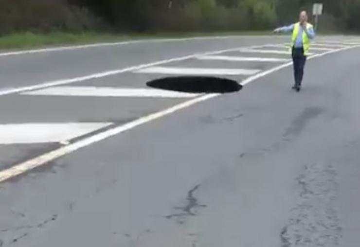 Un conductor sinaliza o enorme buraco que apareceu no medio da estrada Santiago - Noia 