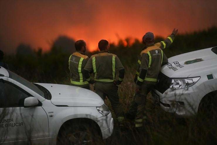 Varios axentes de emerxencias observan o incendio forestal, a 18 de agosto de 2023, en Palas de Rei, Lugo, Galicia (España). O incendio forestal, que se iniciou a tarde de hoxe e viuse avivado polo vento, rolda, segundo a Consellería de Medi. Carlos Castro - Europa Press