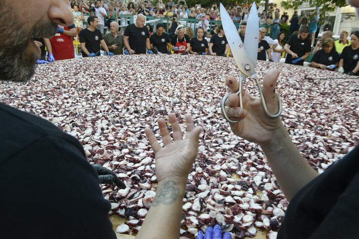 Unha persoa sostén unhas tesoiras fronte a quilos de polbo no Carballiño 