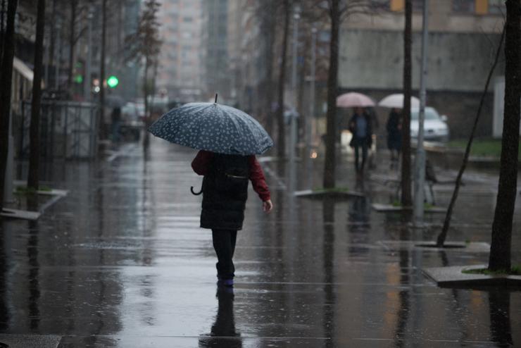 Unha persoa con paraugas para protexerse da choiva camiña pola Rua Loureiro Crespo 