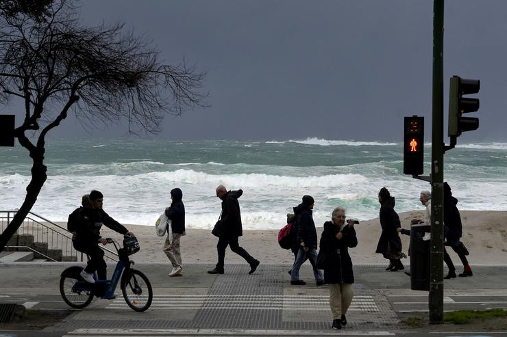 Varias persoas camiñan na Coruña diante das ondas causadas por un temporal e borrasca que trae chuvia e vento / M. Dylan - Europa Press