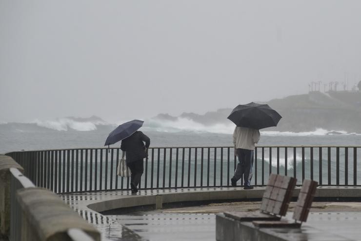 Dúas persoas camiñan cun paraugas á beira da praia do Orzán na Coruña 
