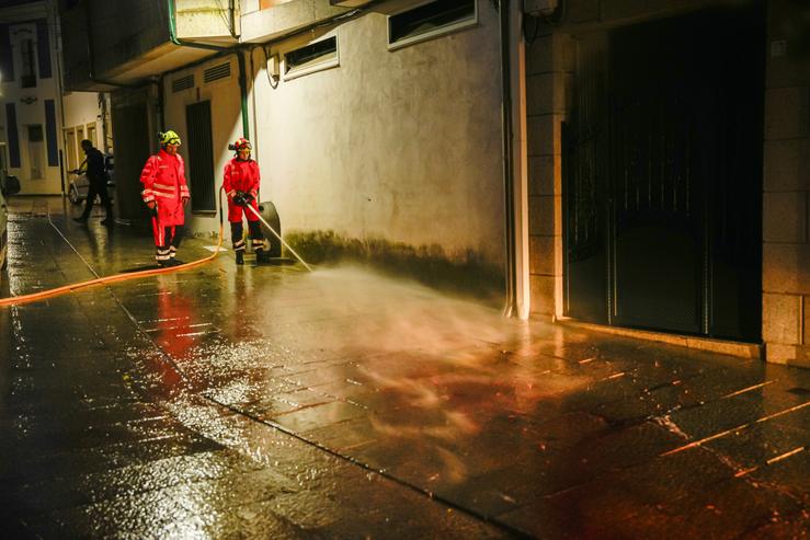 Bombeiros limpan a rúa de Vilaxoán de Arousa, en Vilagarcía de Arousa, onde un home asasinou supostamente ao seu cuñado dunha puñalada na tarde deste venres, 26 de maio de 2024 / ADRIAN IRAGO / Europa Press