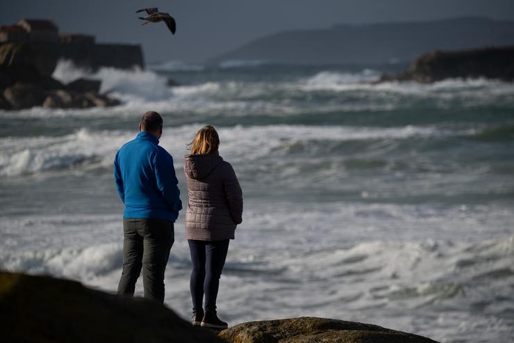 Dúas persoas observan o mar con ondas polo temporal, na praia da Lanzada / Elena Fernández / Europa Press